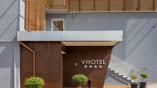 A modern hotel entrance with a staircase leading to an upper level, a sign reading "VHOTEL," and three potted trees in front. - V Hotel (Ancona)