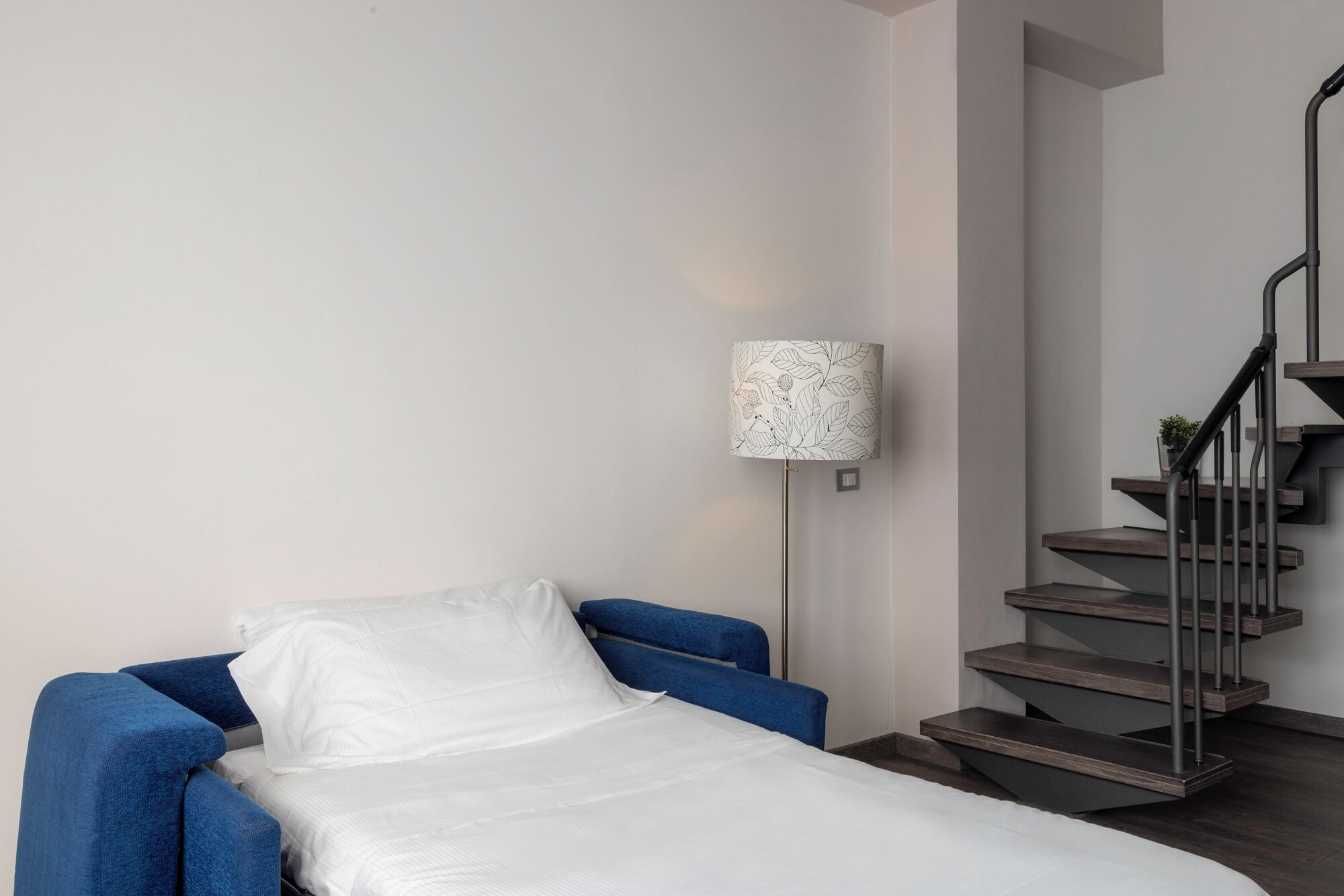 Un dormitorio con una cama individual, un sillón azul, una lámpara de pie y una escalera.