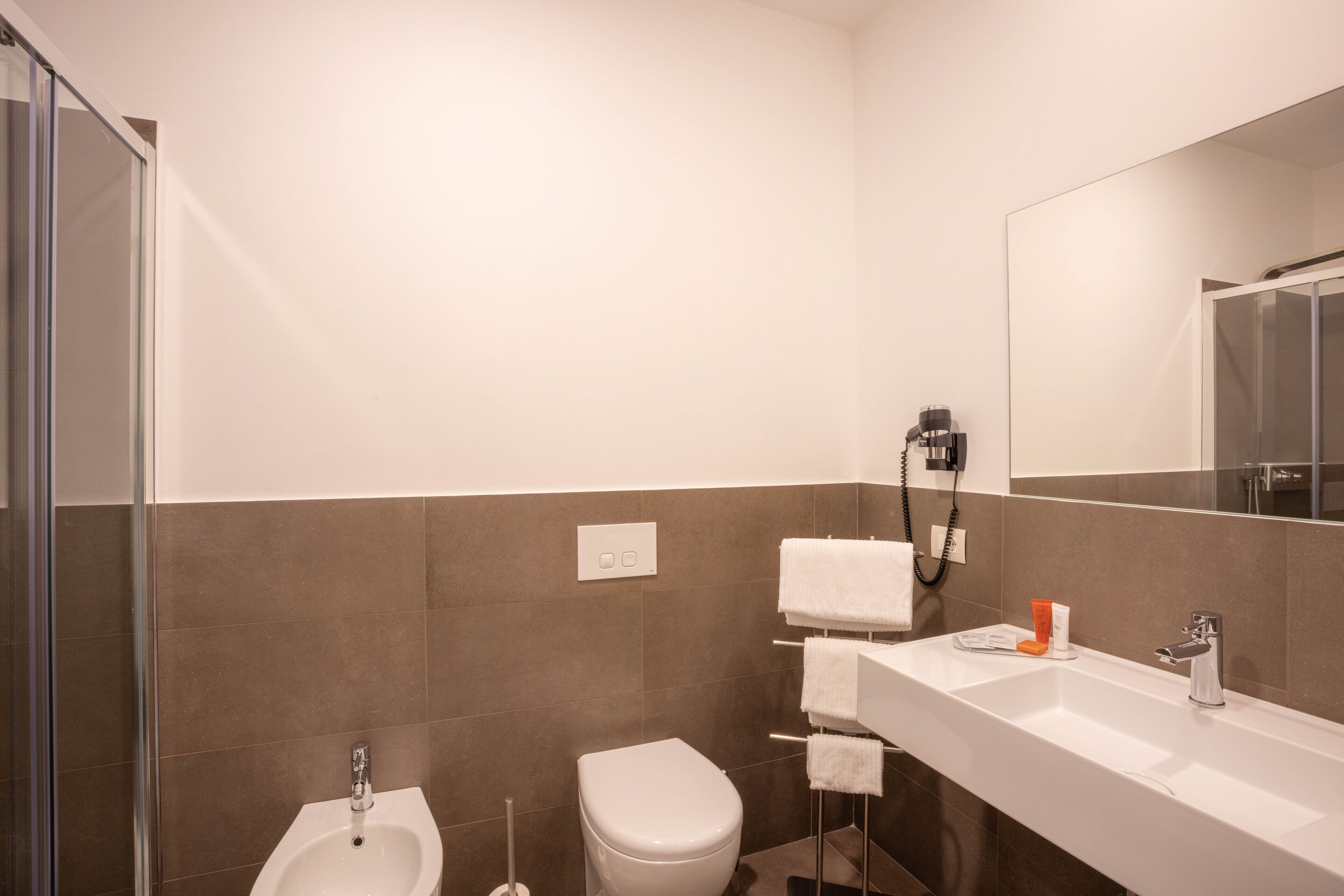 Un baño moderno con ducha, inodoro, bidé y un espejo grande sobre el lavamanos.