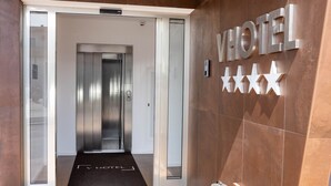 A hotel reception area with a modern design, featuring a reception desk, a wall-mounted sign with the word "HOTEL" and stars, and an elevator in the background. - V Hotel (Ancona)