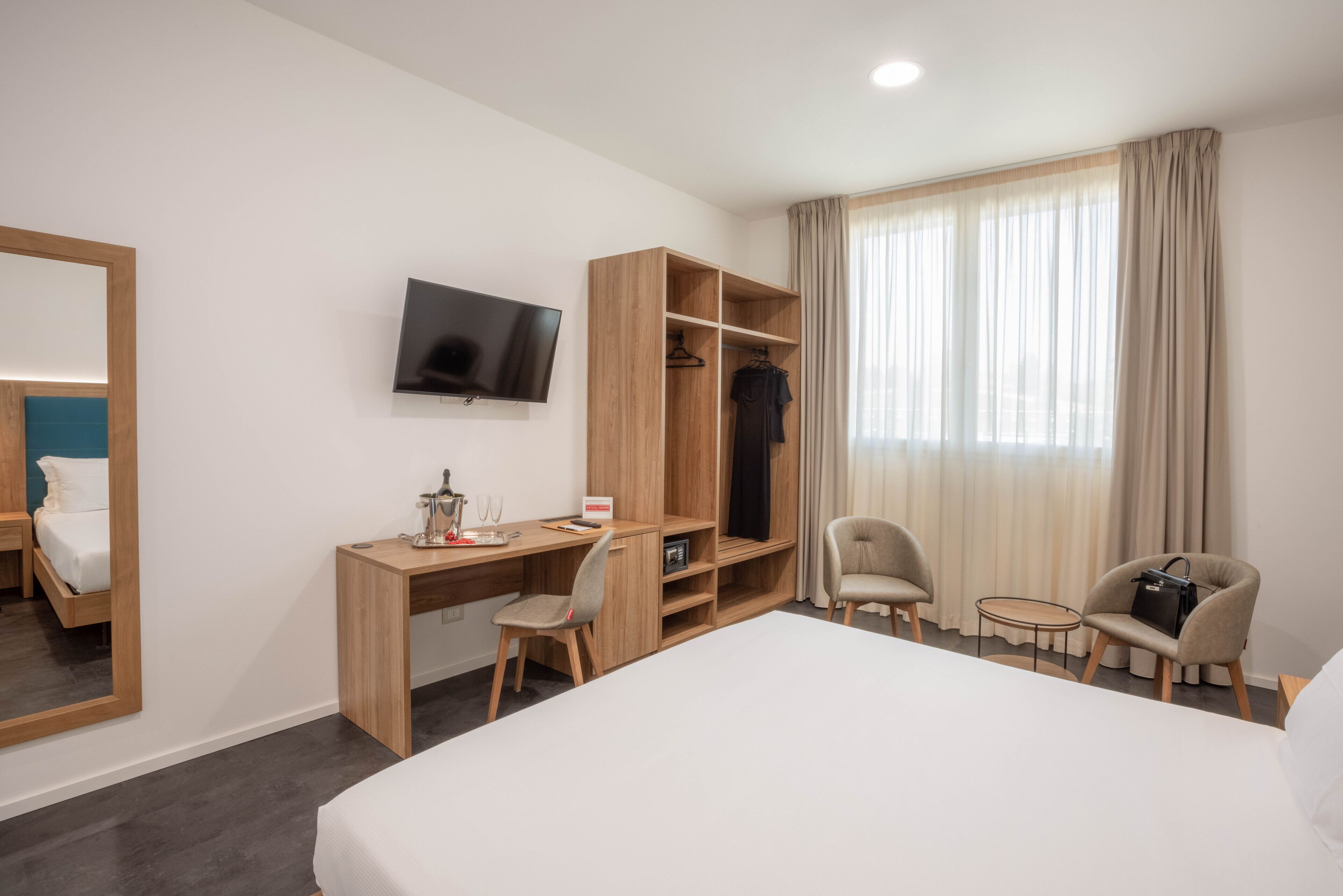 A hotel room with a bed, a desk, a chair, a TV, a wardrobe, and a window with curtains.