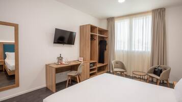 A hotel room with a bed, a desk, a chair, a TV, a wardrobe, and a window with curtains.