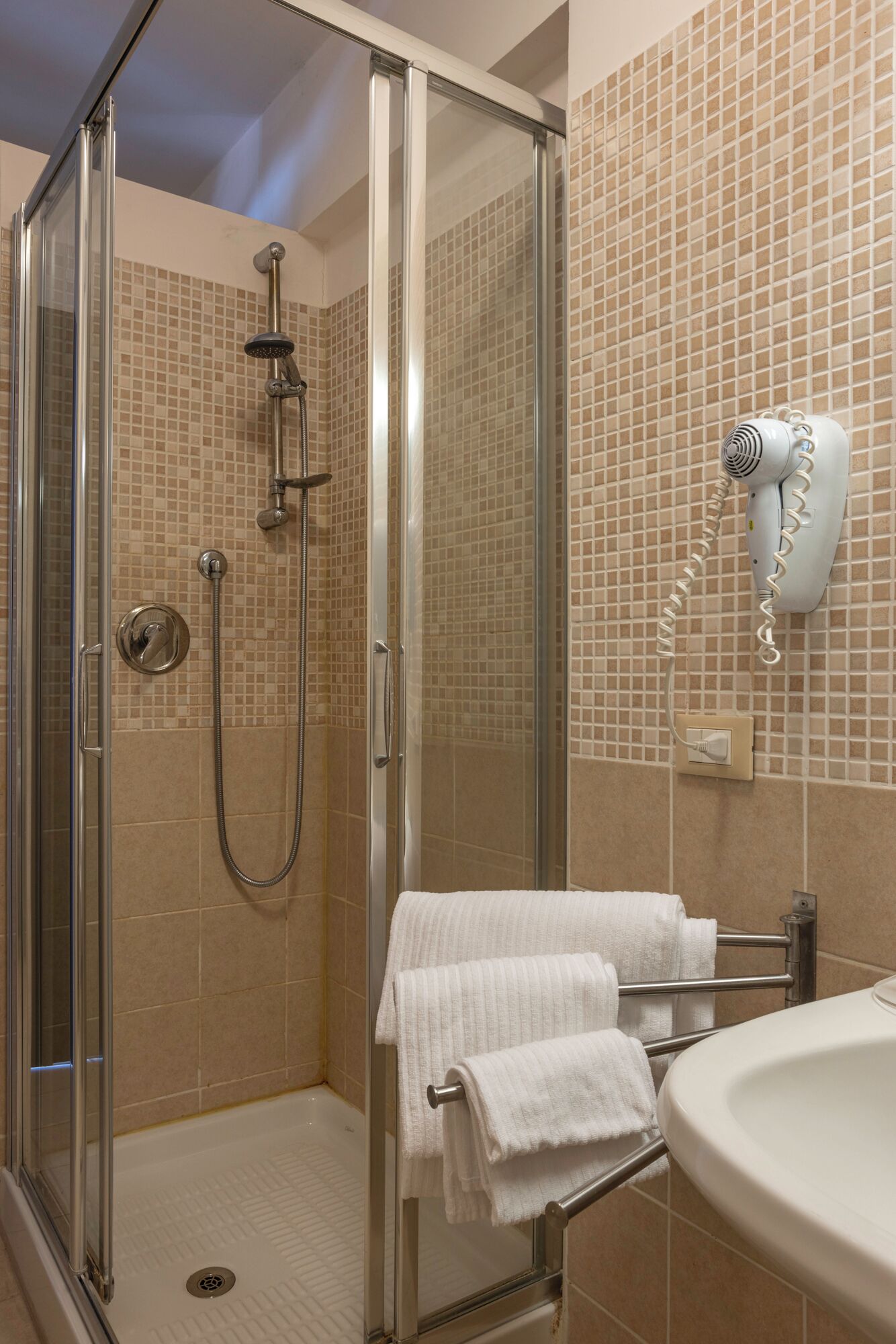 Une salle de bain moderne dotée d’une douche à parois de verre, d’un sèche-cheveux fixé au mur et d’un lavabo avec un porte-serviettes.