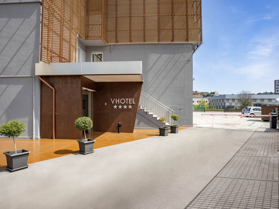 A modern hotel entrance with a staircase leading to the second floor, potted plants, and a clear sky.
