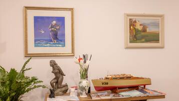A table with a framed painting, a vase with flowers, a small boat model, and a potted plant.