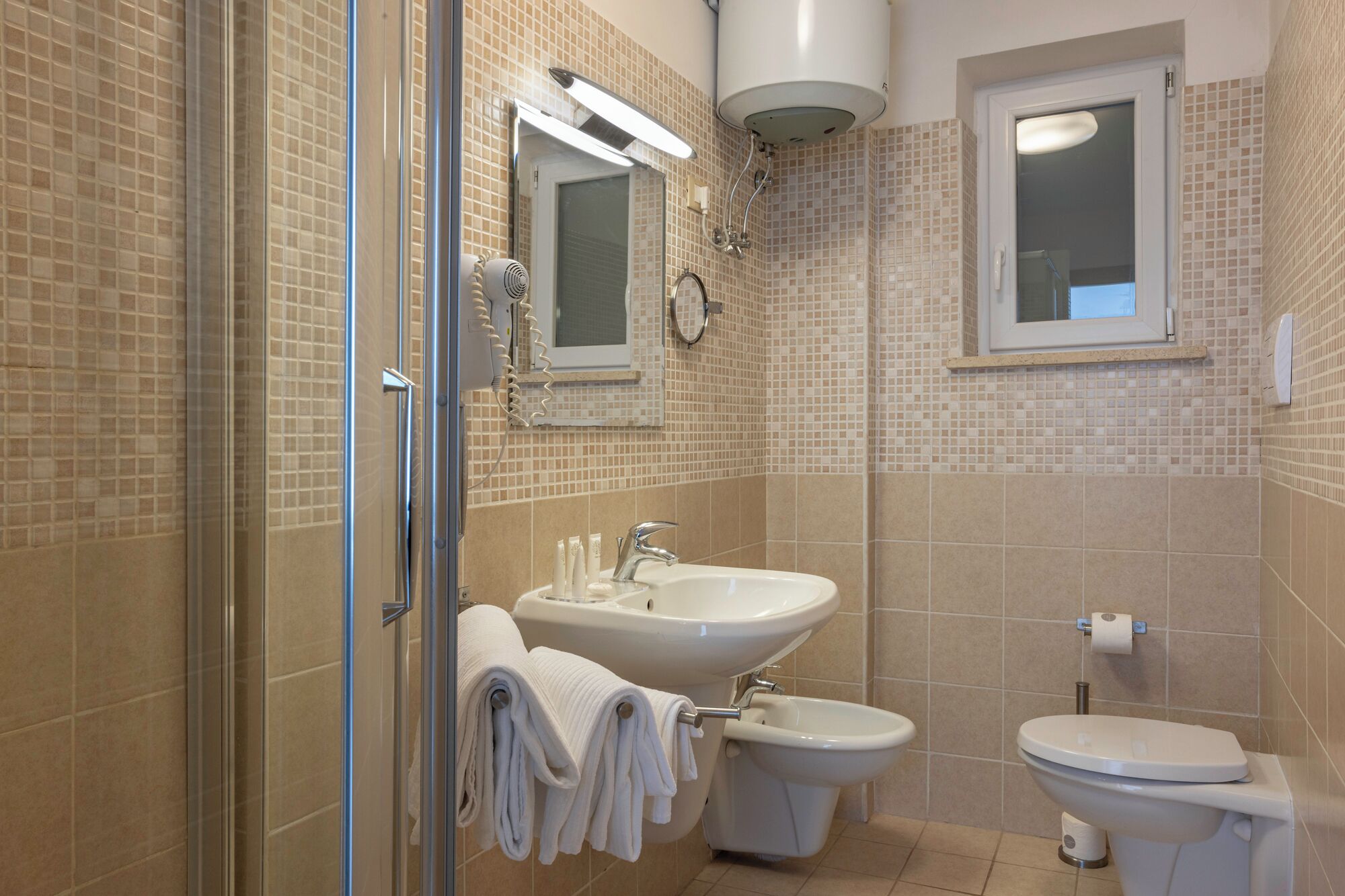 Un baño con cabina de ducha de vidrio, lavamanos, un bidé y un inodoro.