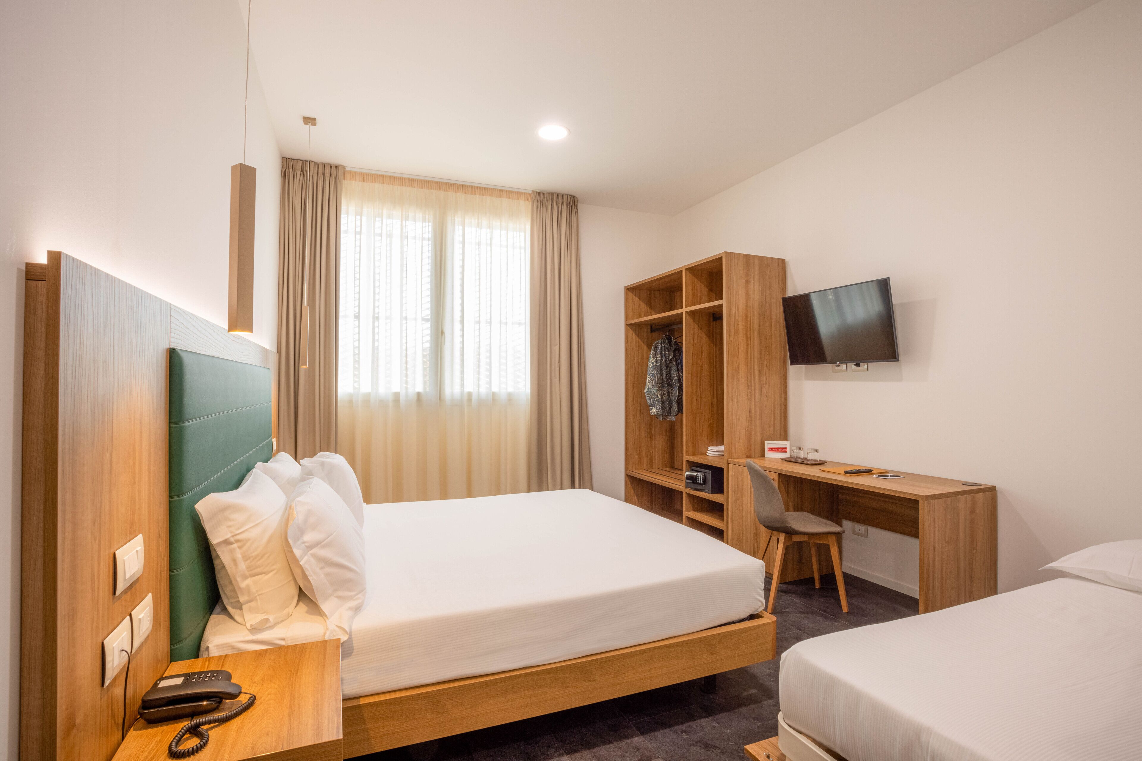 Habitació d'hotel amb llit, escriptori, televisió i armari.