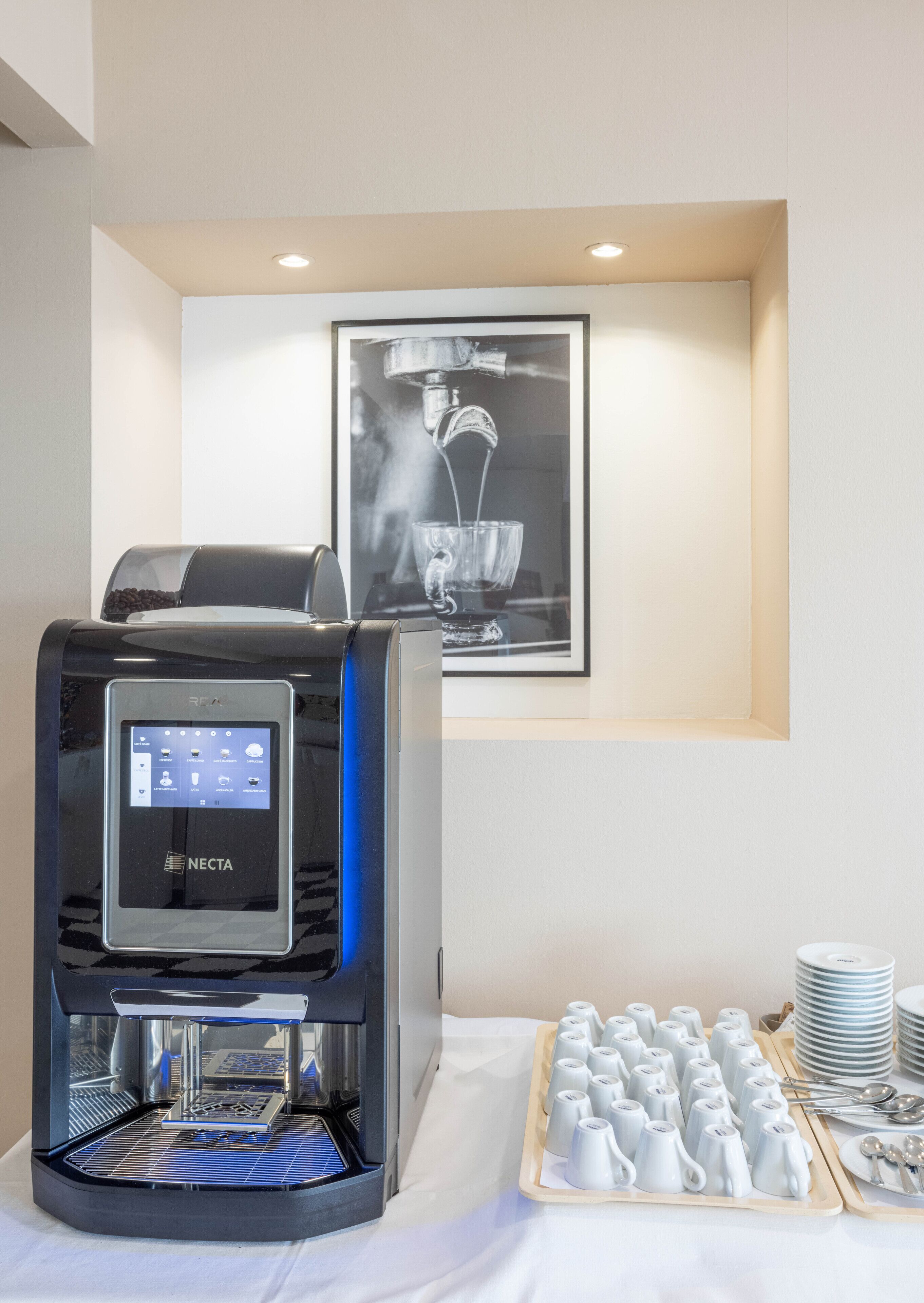 A coffee machine with a digital display, a coffee cup dispenser, and a tray of disposable cups.