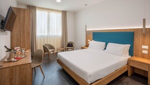 A hotel room with a bed, bedside tables, a desk with a chair, a TV mounted on the wall, and a window with curtains. - V Hotel (Ancona)