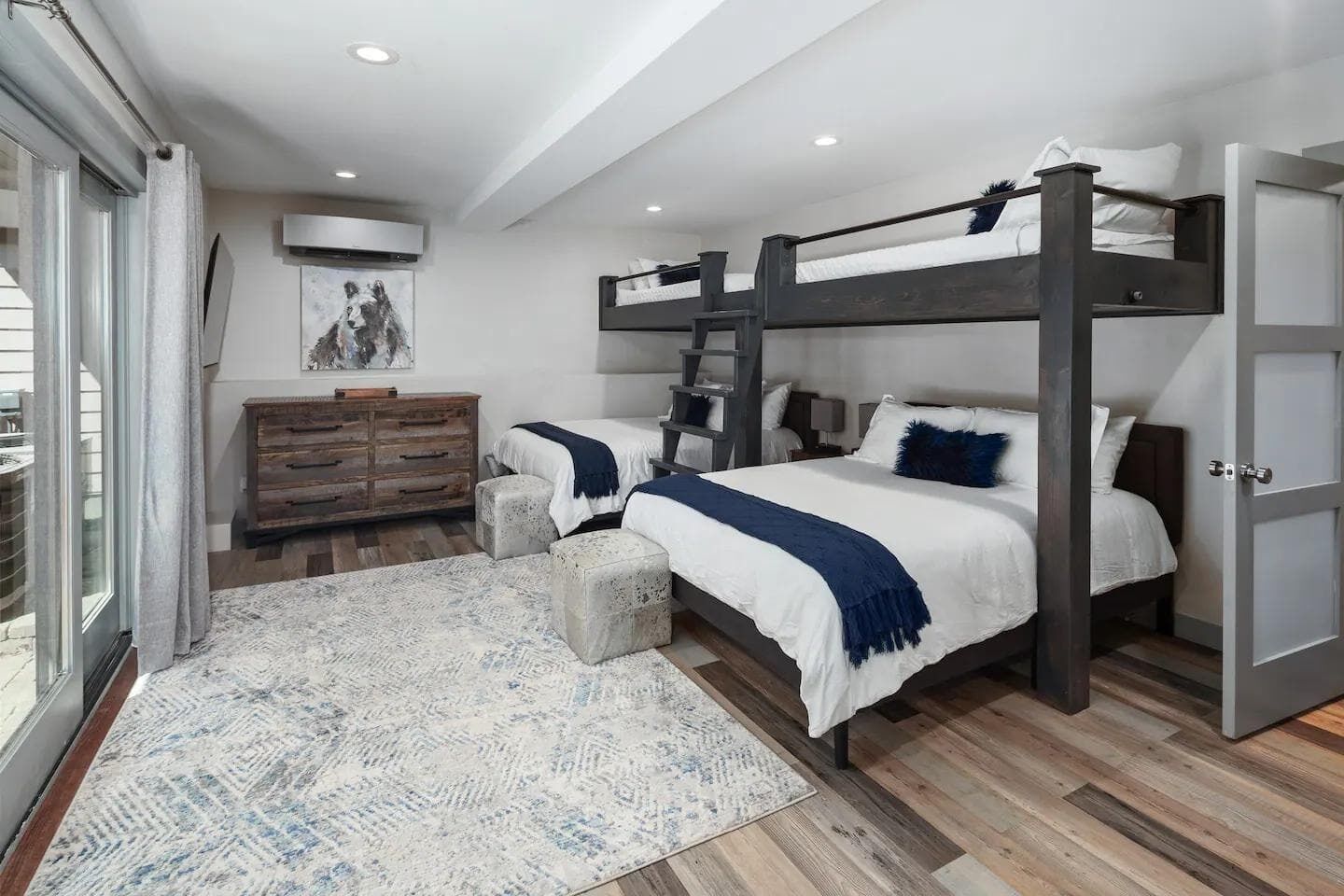Une chambre avec des lits superposés, une commode en bois, un tapis et un tableau accroché au mur.