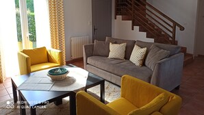 Een woonkamer met een bank, gele fauteuils, een bijzettafeltje en een trap.