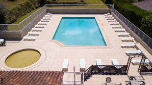 Zwembad met ligbedden en een kleine jacuzzi, omringd door een betegeld zonnedek en een lage stenen muur.