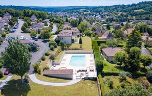 Ett flygbildsbild av ett bostadsområde med en swimmingpool, hus och grönområden.