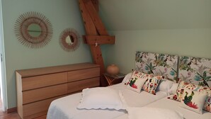 Een slaapkamer met een houten dressoir, een bed met bloemenkussens en twee spiegelwanden.
