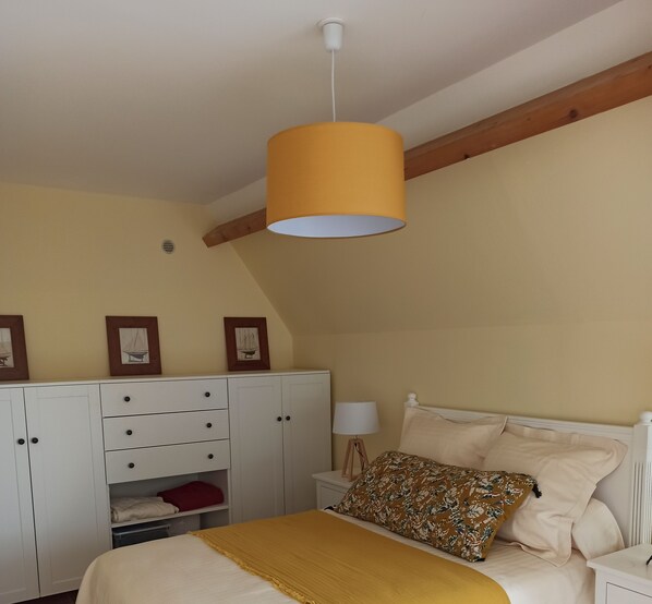 A bedroom with a bed, a wardrobe, a nightstand, and a hanging lamp.