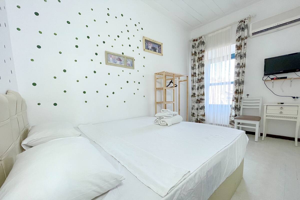 A bedroom with a bed, a desk, a chair, and a TV.