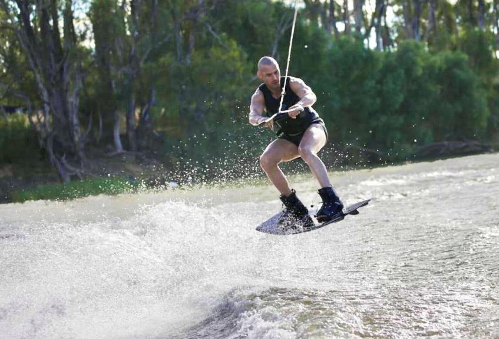 En person som åker wakeboard på en sjö eller ett annat vattendrag, med träd i bakgrunden.