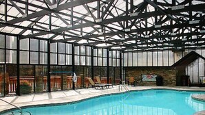 Une piscine intérieure dotée d’un toit en verre, de chaises longues et d’un mur en pierre.