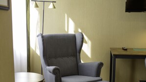 A hotel room with a grey armchair, a small round table, a TV on a wooden stand, and a bed with a green bedspread. - Stadthotel König Albert (Zittau)