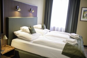 A neatly made bed with white linens and pillows, a bedside table with a lamp, and a headboard with built-in lighting. - Stadthotel König Albert (Zittau)