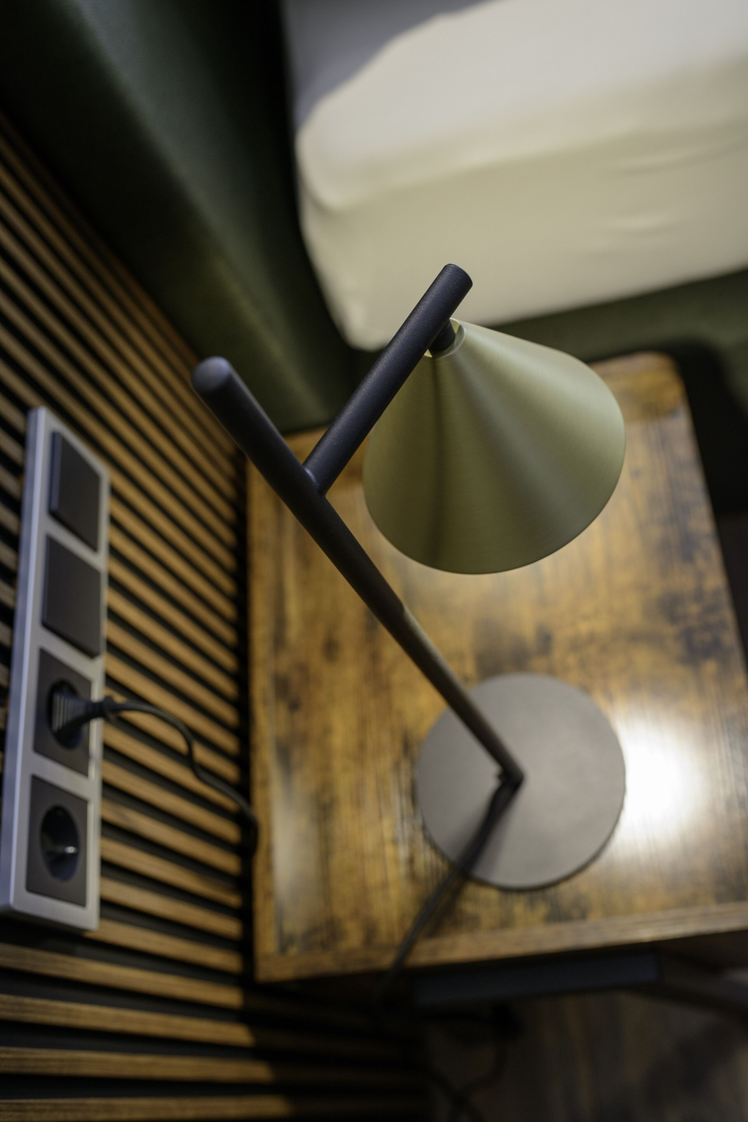 Una lámpara moderna con base metálica y un brazo curvo sobre una mesa de madera.