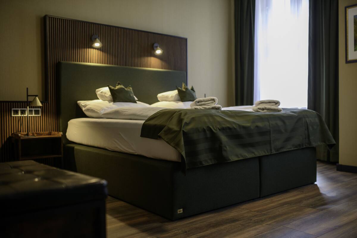 Una habitación de hotel moderna con una cama grande, una mesita de noche y otra mesita auxiliar.