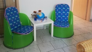 Une pièce comprenant deux chaises vertes, une petite table blanche et une œuvre d’art murale.