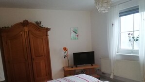 Une chambre à coucher avec un lit, une armoire en bois, un meuble pour la télévision et une fenêtre avec des rideaux.