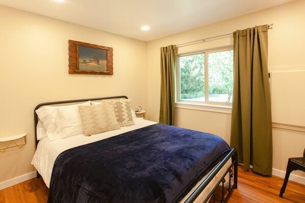 Une chambre à coucher avec un lit, une table de chevet, une fenêtre avec des rideaux et un tableau accroché au mur.