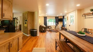 Un vaste espace de vie comprenant un coin repas avec une table en bois, un canapé et une cuisine équipée de meubles et d’appareils électroménagers en bois.