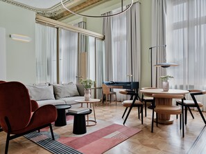 A modern living room with a sofa, chairs, a coffee table, and a dining area with a table and chairs. - Hotel Altus Palace - Destigo Hotels (Wroclaw)