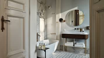 A bathroom with a marble wall, a round mirror, a white bathtub, and a black floor pattern.