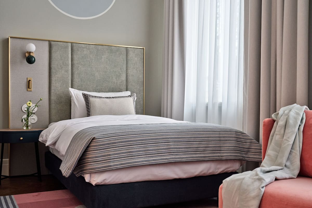 A modern bedroom with a bed, bedside table, lamp, and a view of the outdoors through sheer curtains.