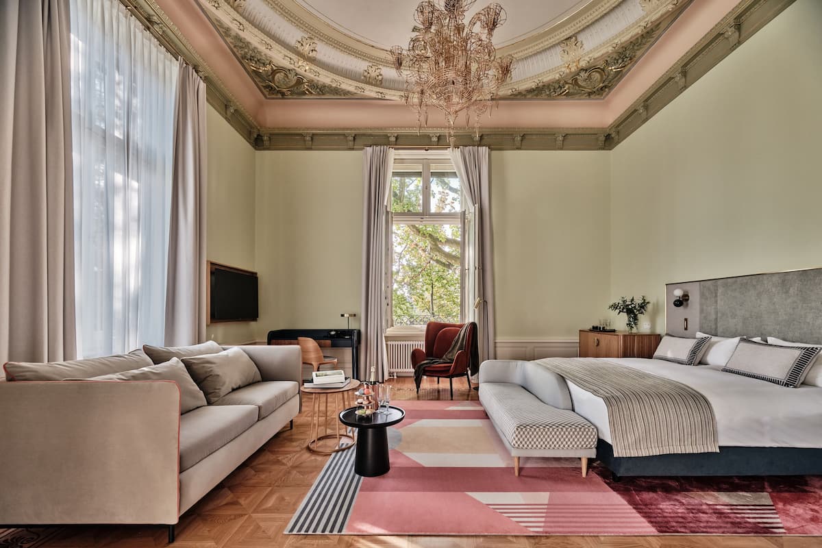A spacious room with a large bed, a sofa, a television, and a window with curtains.