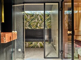 A modern bathroom with a glass door, a shower area, and a tiled wall with a leaf pattern.
