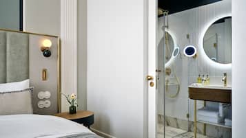 A modern bathroom with a glass-enclosed shower, a round mirror, and a vanity with toiletries.