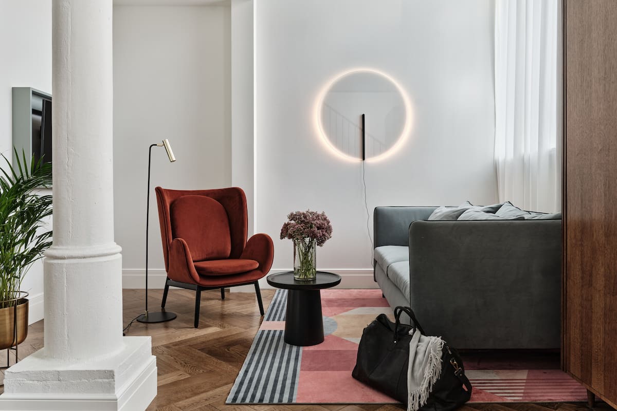 A modern living room with a red armchair, grey sofa, and a round wall light.