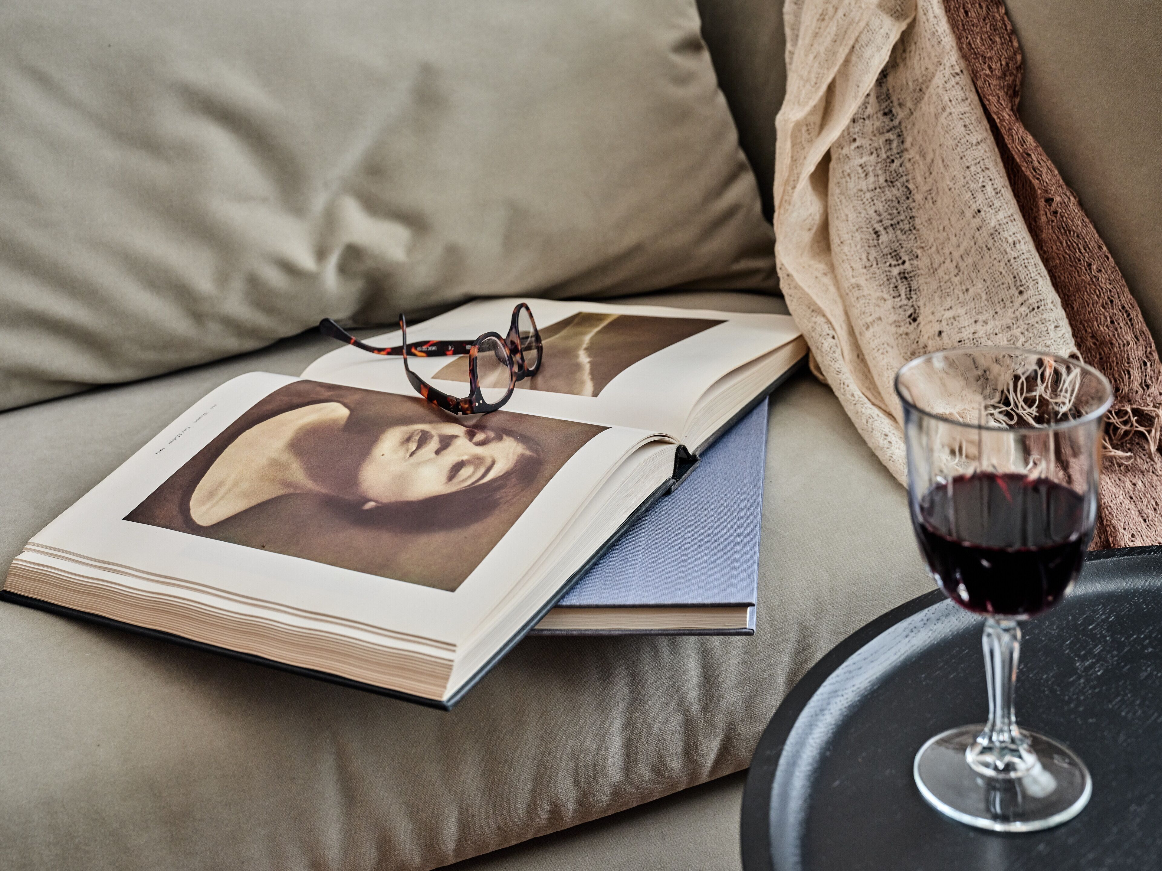 Ein Buch, eine Brille und ein Glas Rotwein auf einer Couch.