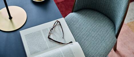 A room with a blue armchair, a table with a book and glasses, and a coffee cup on a saucer.