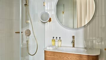 A bathroom with a wooden vanity, a round mirror, and a shower with a gold showerhead.