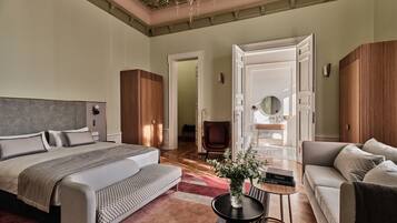 Un dormitorio amplio con una cama grande, un sofá, una mesita con un jarrón, y un baño visible a través de una puerta abierta.