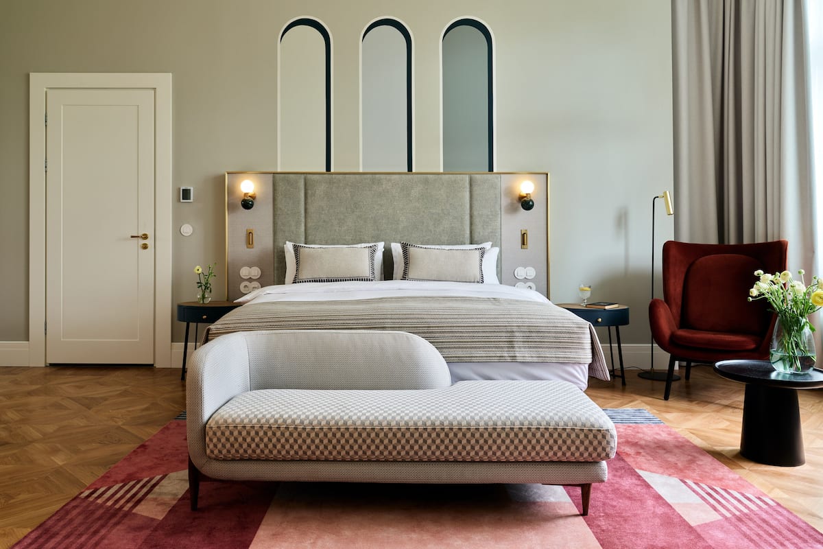 A modern bedroom with a large bed, a red armchair, and a nightstand with a lamp.
