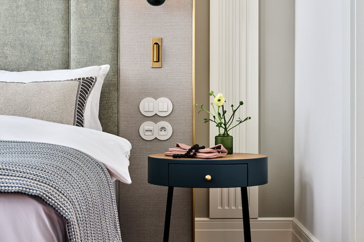 A bedroom with a bed, a bedside table with a lamp, and a wall-mounted light fixture.
