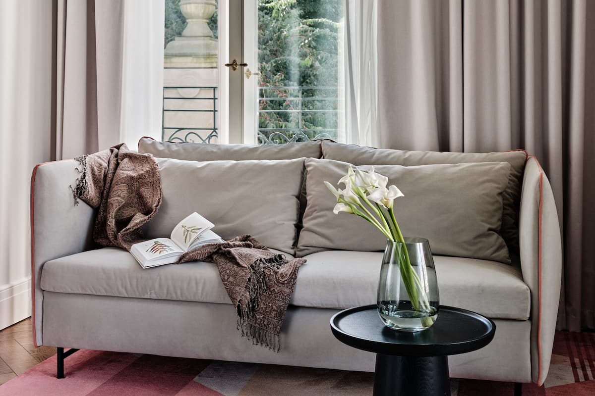 A modern living room with a sofa, a small round table, and a view of a garden through a large window.