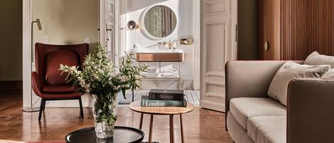 A living room with a sofa, a chair, a coffee table with books, and a vase with flowers.