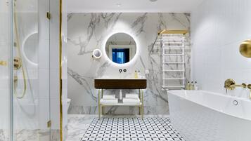 A modern bathroom with a marble wall, a round mirror, a wooden vanity, a white bathtub, and a patterned floor.