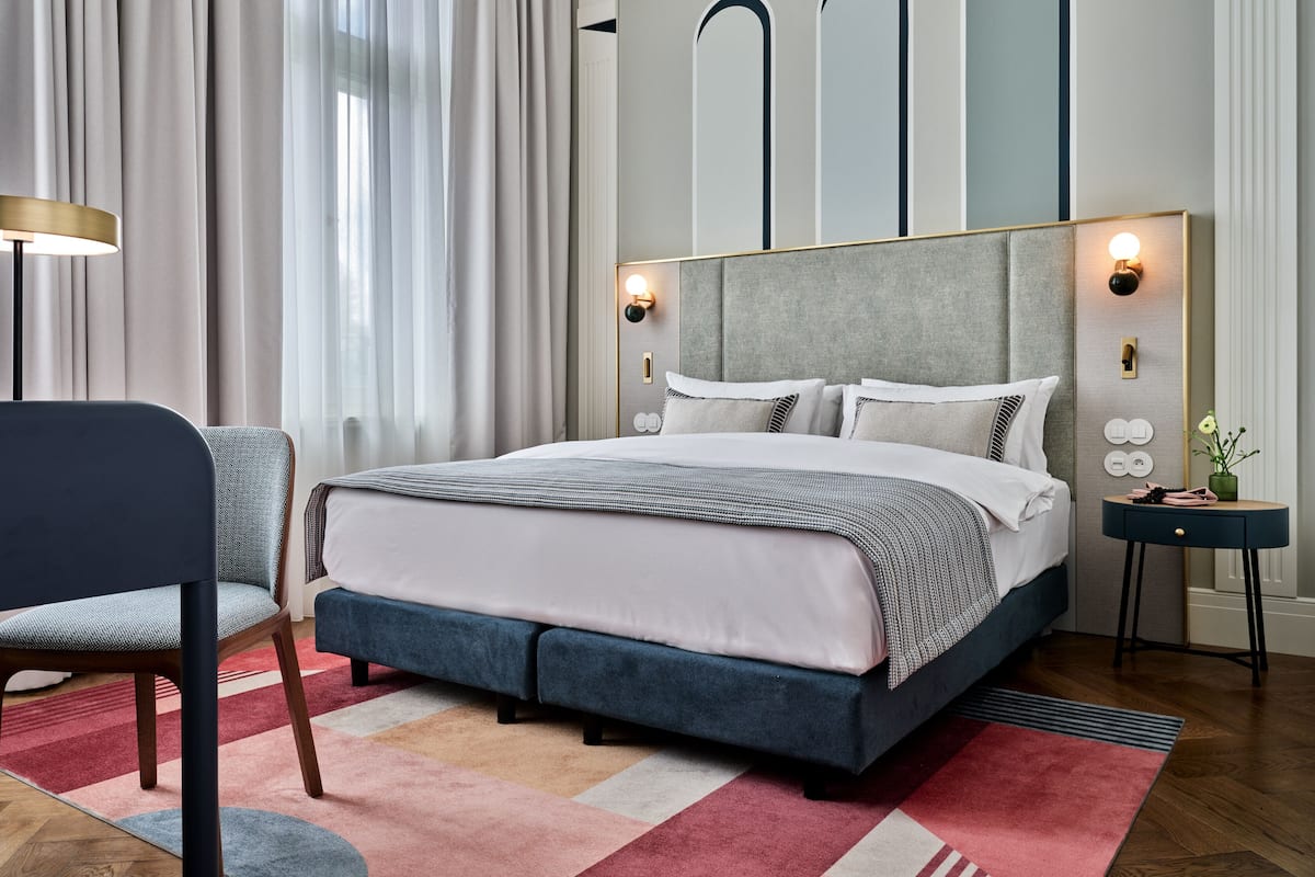 A modern bedroom with a large bed, a nightstand, a chair, and a wall-mounted light fixture.