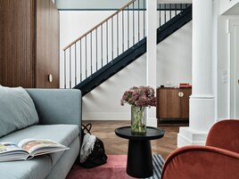 A modern living room with a grey sofa, a black coffee table with a vase of flowers, a wooden cabinet, and a staircase with black railings.