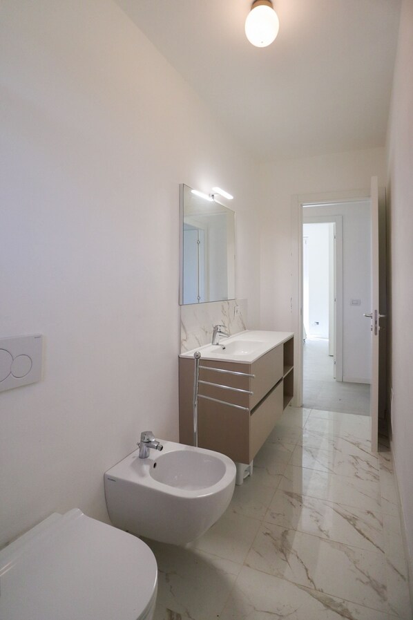 Une salle de bain équipée de toilettes, d’un bidet, d’un lavabo et d’un miroir.