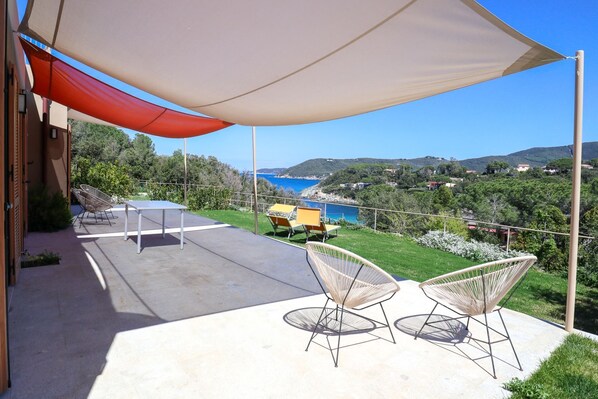 An outdoor patio with a view of the sea, two wicker chairs, a table, and a large canopy. - Luxury apartment with private access to the sea. (Procchio)